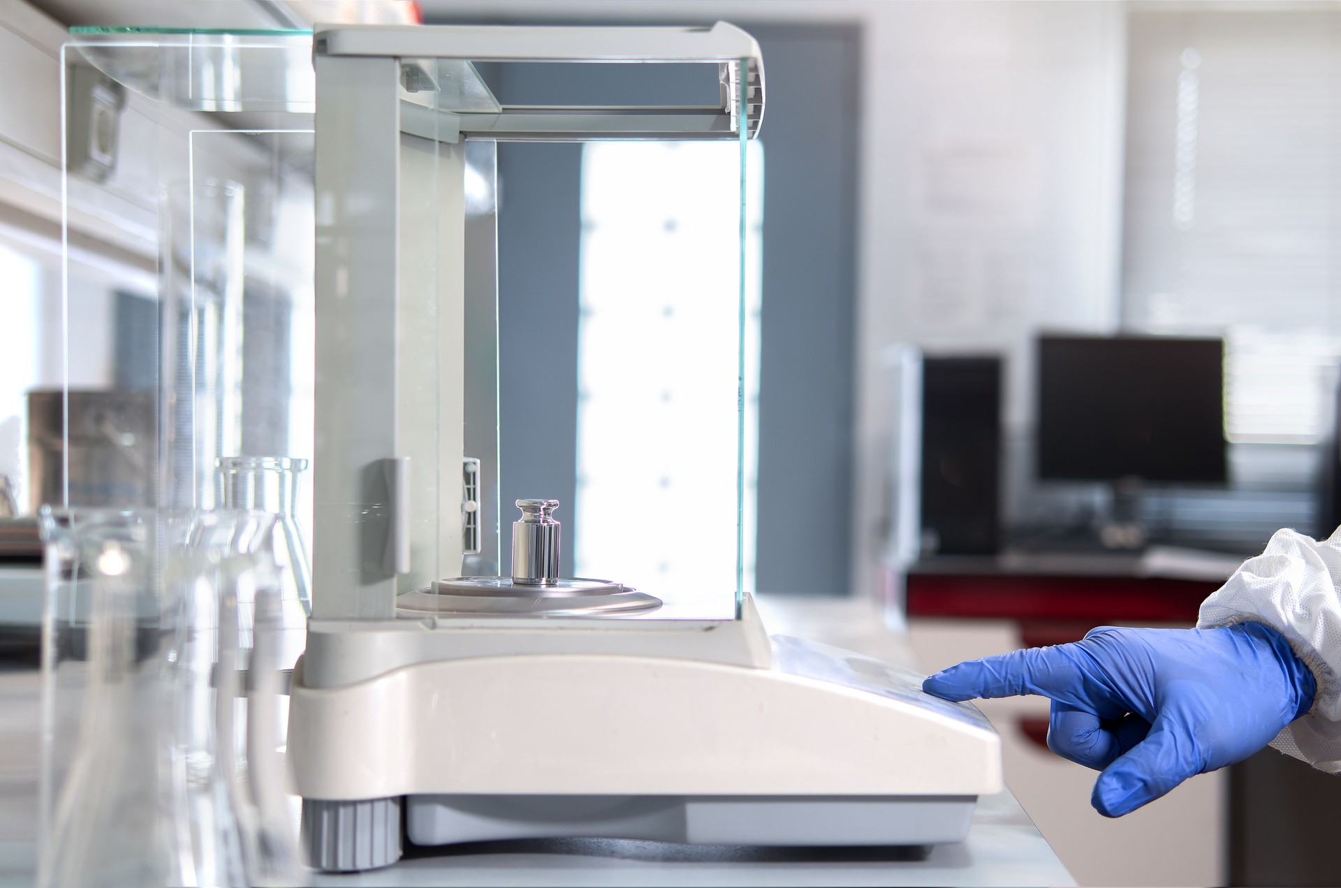 A operator's hand is holding steel calibration weight to place on the analytical balance. Concept of quality control in a laboratory.