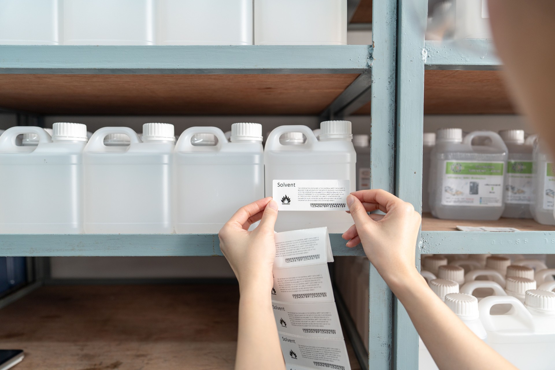Chemist puts a barcode sticker on a plastic bottle containing a solvent.